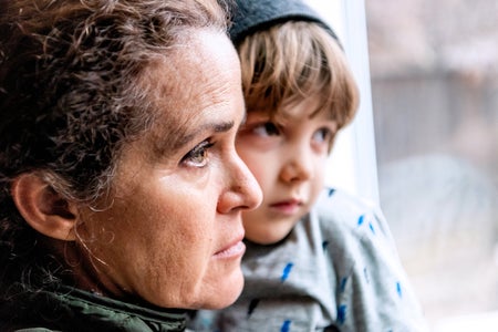 Concerned mother holding son looks out her window.