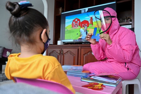 A teacher in a biosecurity suit gives a lesson to a girl in her home in Cali, Colombia.