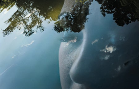 Face of a woman reflected a on body of water.