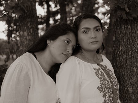 Isabel Hernandez rests her head on Magdalene Quintero's shoulder. Both wear white.