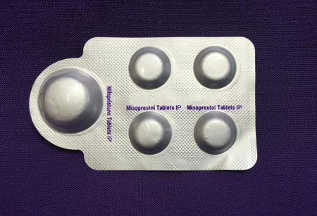 Combination pack of mifepristone (L) and misoprostol tablets on purple bsckground.