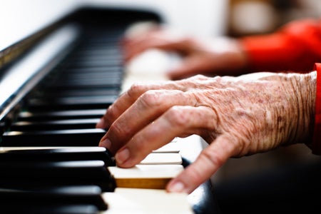 Old wrinkled hands with red cuffs playing the piano.