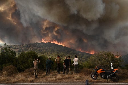 People look at heavy wildfire smoke in mountaneous area taking photos and parked motorcycle.