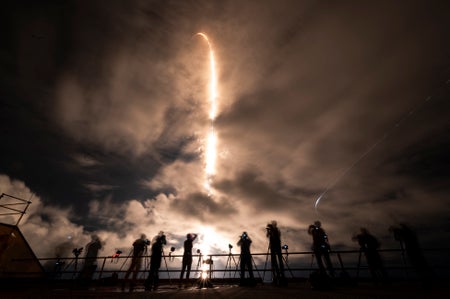 SpaceX Crew Dragon capsule atop of Falcon 9 rockets launching while photographers shooting on ground.